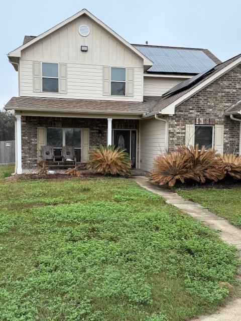 7 N Pine Rd, Texas City, TX 77591 - view of front of home featuring a front lawn, roof mounted solar panels, a porch, and board and batten siding