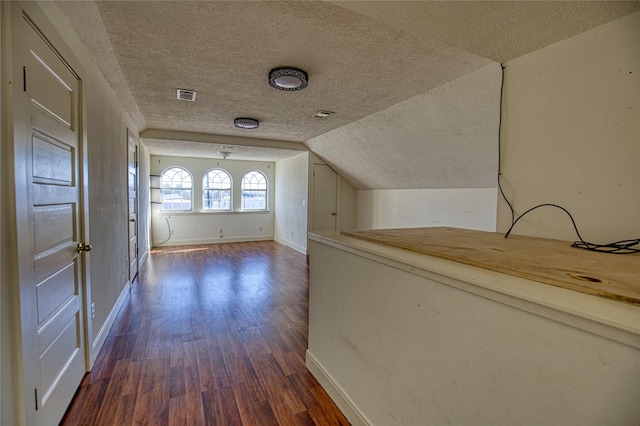 hallway featuring dark hardwood / wood-style flooring, vaulted ceiling, and a textured ceiling