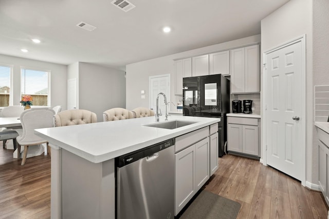 kitchen featuring sink, gray cabinetry, a kitchen island with sink, stainless steel dishwasher, and light hardwood / wood-style flooring