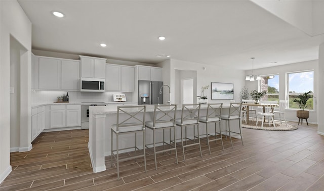 kitchen with a breakfast bar, stove, white cabinetry, an island with sink, and stainless steel fridge with ice dispenser