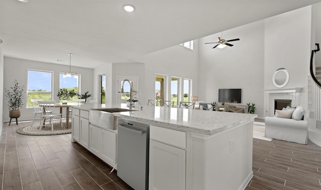 kitchen with white cabinetry, light stone counters, hanging light fixtures, stainless steel dishwasher, and an island with sink