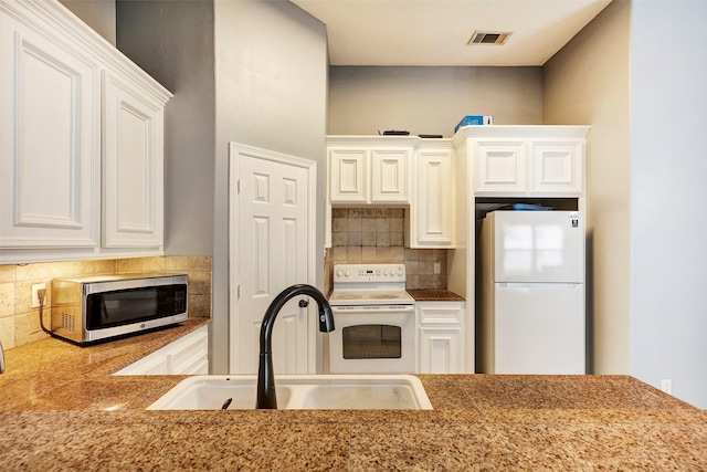 kitchen with sink, tasteful backsplash, white appliances, a tiled fireplace, and white cabinets