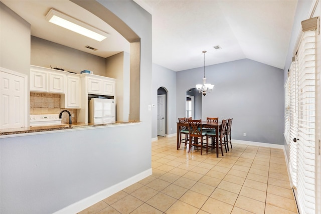 kitchen with light tile patterned flooring, vaulted ceiling, refrigerator, white cabinetry, and decorative backsplash