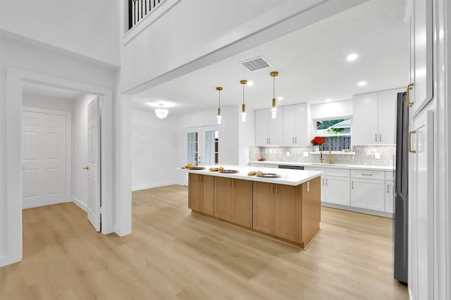 kitchen with pendant lighting, sink, white cabinetry, a center island, and light wood-type flooring