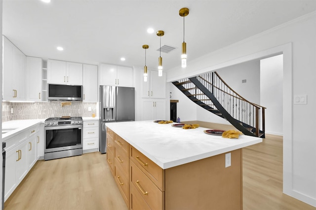 kitchen with white cabinetry, a center island, hanging light fixtures, appliances with stainless steel finishes, and light hardwood / wood-style floors