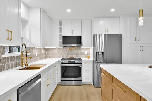 kitchen featuring appliances with stainless steel finishes, white cabinetry, sink, hanging light fixtures, and light stone counters