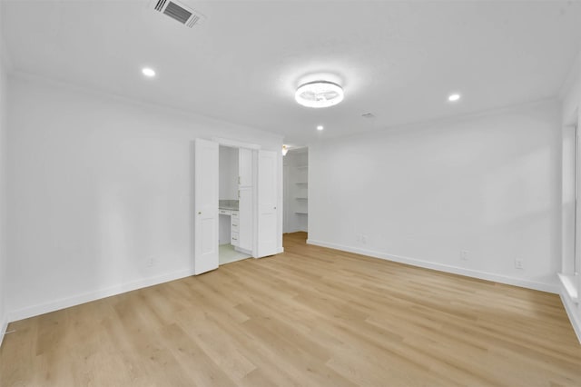 empty room with a walk in closet, ensuite bath, and light hardwood / wood-style flooring