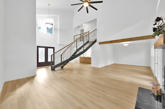 unfurnished living room with french doors, a towering ceiling, and light hardwood / wood-style floors