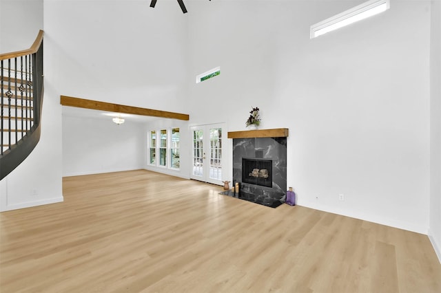 unfurnished living room with french doors, a high ceiling, a high end fireplace, and light hardwood / wood-style flooring