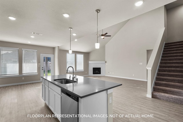 kitchen with dark countertops, open floor plan, stainless steel dishwasher, white cabinetry, and a sink