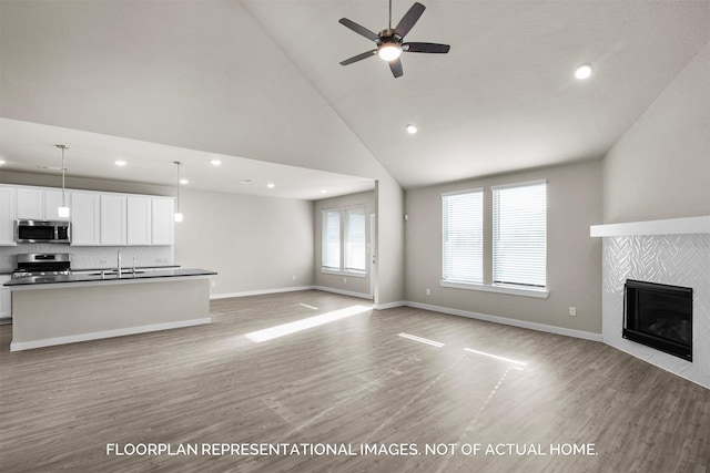 unfurnished living room with high vaulted ceiling, sink, a tiled fireplace, and light hardwood / wood-style floors