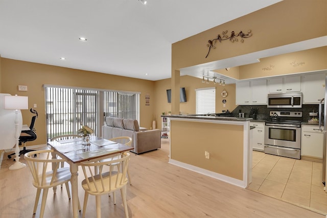 kitchen featuring dark countertops, backsplash, appliances with stainless steel finishes, open floor plan, and white cabinetry