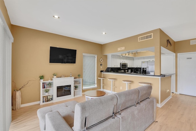 living area featuring recessed lighting, visible vents, a glass covered fireplace, light wood-type flooring, and baseboards