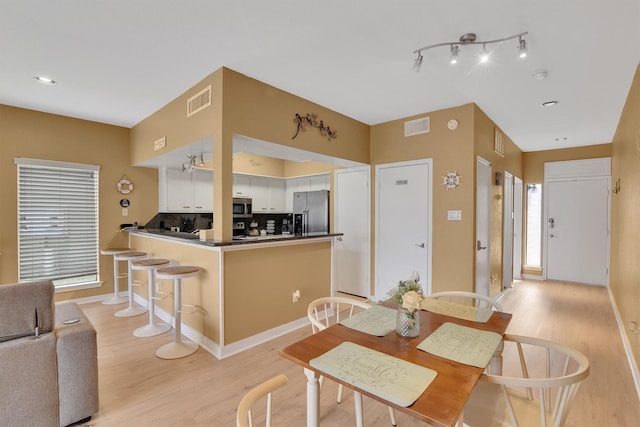 dining room with light wood-type flooring, visible vents, and baseboards