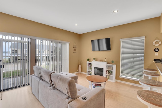 living room with light wood finished floors, recessed lighting, baseboards, and a glass covered fireplace