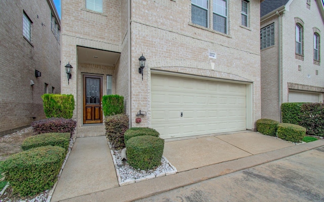 doorway to property with a garage, brick siding, and driveway