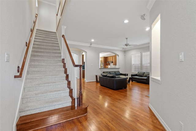 stairway with ceiling fan, ornamental molding, and wood-type flooring