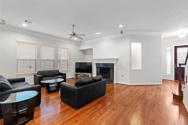 living room with ornamental molding, light hardwood / wood-style floors, a premium fireplace, and ceiling fan