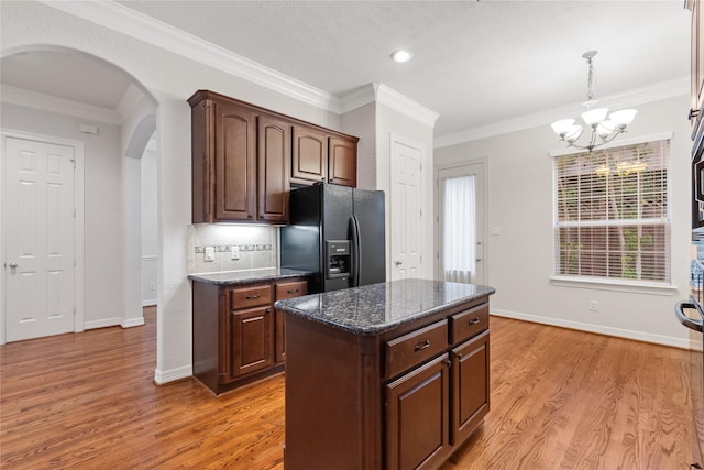 kitchen with dark brown cabinetry, a kitchen island, black fridge with ice dispenser, and dark stone counters