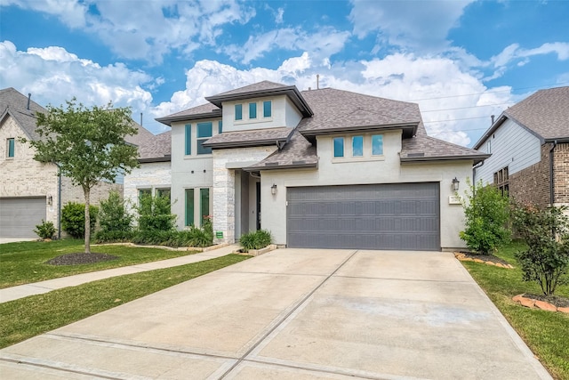 prairie-style home featuring a garage, a shingled roof, concrete driveway, stucco siding, and a front yard