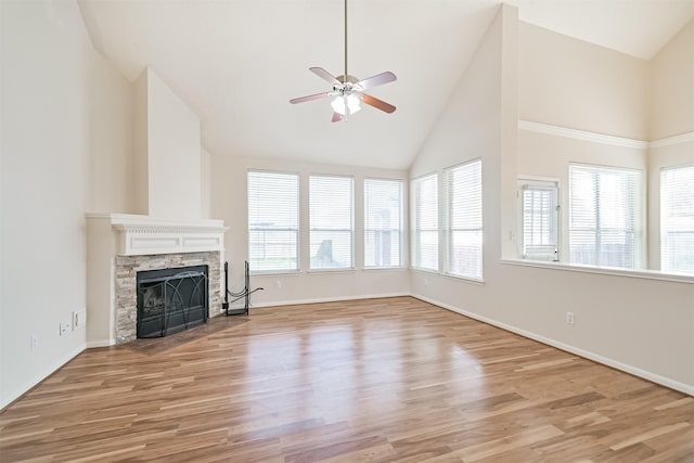 unfurnished living room featuring ceiling fan, high vaulted ceiling, a stone fireplace, and light hardwood / wood-style floors