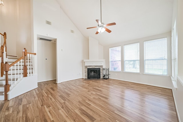 unfurnished living room featuring a stone fireplace, high vaulted ceiling, ceiling fan, and light hardwood / wood-style flooring