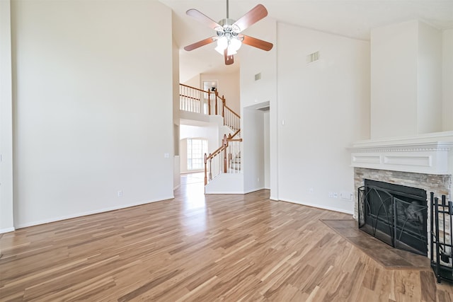 unfurnished living room featuring ceiling fan, high vaulted ceiling, a stone fireplace, and light hardwood / wood-style floors