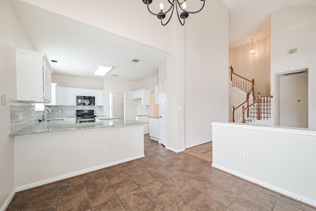 kitchen featuring stainless steel range oven, sink, white cabinetry, light stone counters, and kitchen peninsula