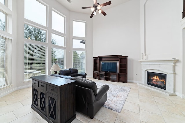 living area featuring a glass covered fireplace, light tile patterned floors, a high ceiling, and a ceiling fan