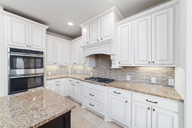 kitchen featuring tasteful backsplash, light tile patterned floors, white cabinets, appliances with stainless steel finishes, and light stone counters