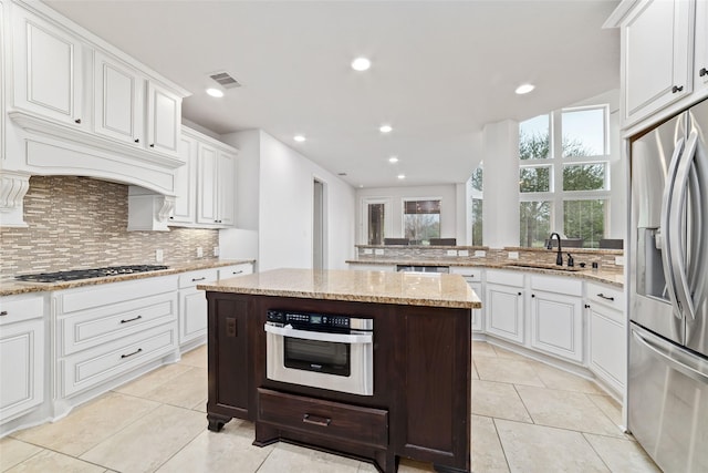 kitchen with light stone counters, visible vents, decorative backsplash, stainless steel appliances, and a sink
