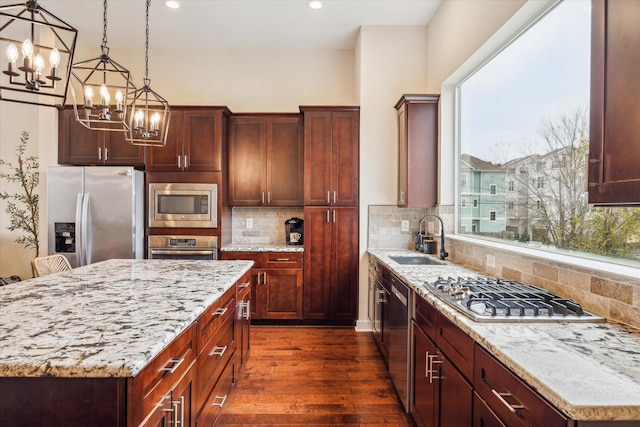 kitchen featuring pendant lighting, sink, a center island, light stone counters, and stainless steel appliances