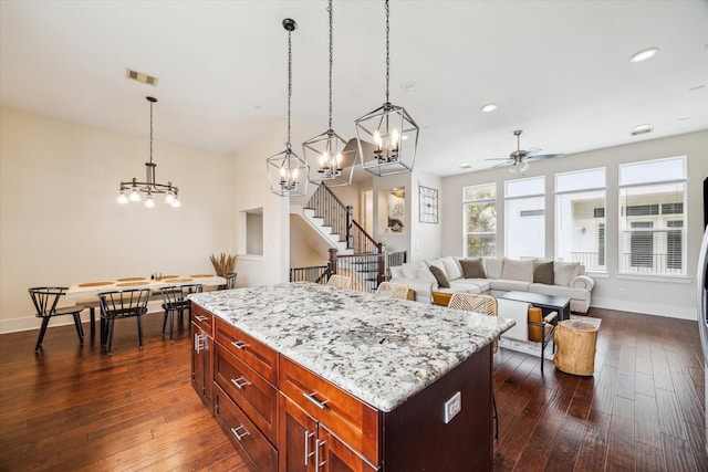 kitchen with light stone countertops, a kitchen island, pendant lighting, and dark hardwood / wood-style flooring