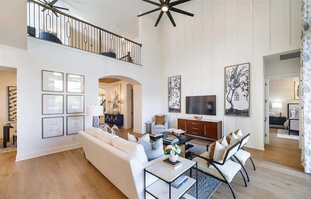 living area with arched walkways, light wood finished floors, a towering ceiling, and ceiling fan
