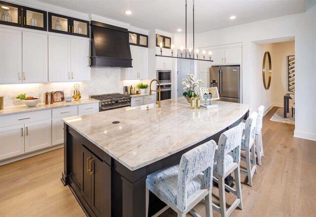 kitchen with a large island, premium appliances, premium range hood, white cabinetry, and decorative backsplash