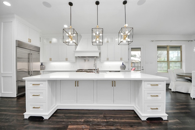 kitchen with light countertops, stainless steel built in refrigerator, a spacious island, and custom range hood