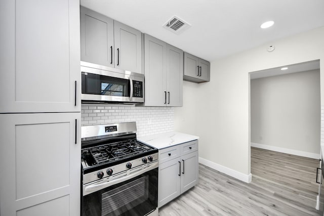 kitchen featuring tasteful backsplash, gray cabinets, visible vents, appliances with stainless steel finishes, and light stone countertops