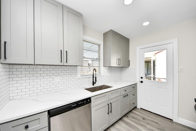 kitchen with stainless steel dishwasher, gray cabinets, a sink, and backsplash