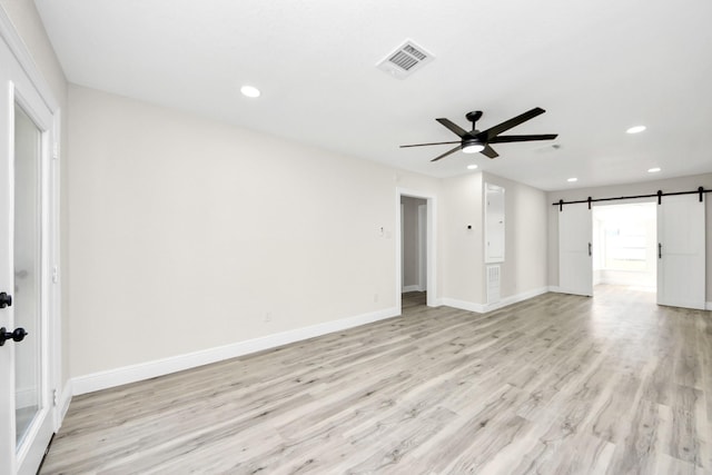 empty room featuring a barn door, recessed lighting, visible vents, baseboards, and light wood finished floors