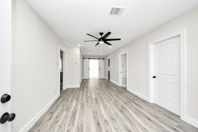 empty room with baseboards, a barn door, visible vents, and light wood-style floors