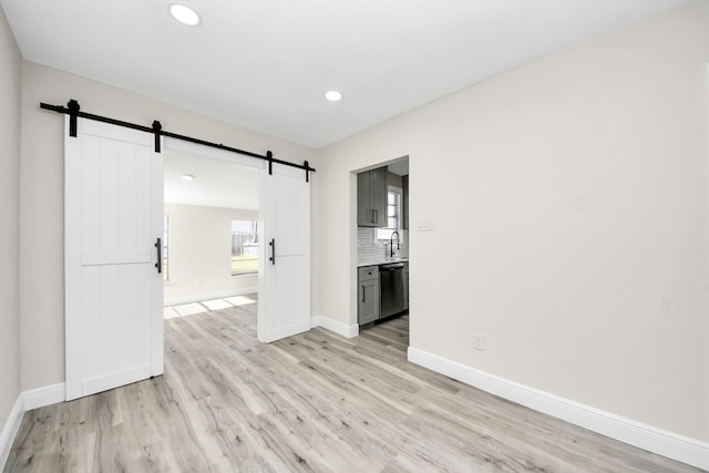 unfurnished room with a barn door, baseboards, light wood-type flooring, a sink, and recessed lighting