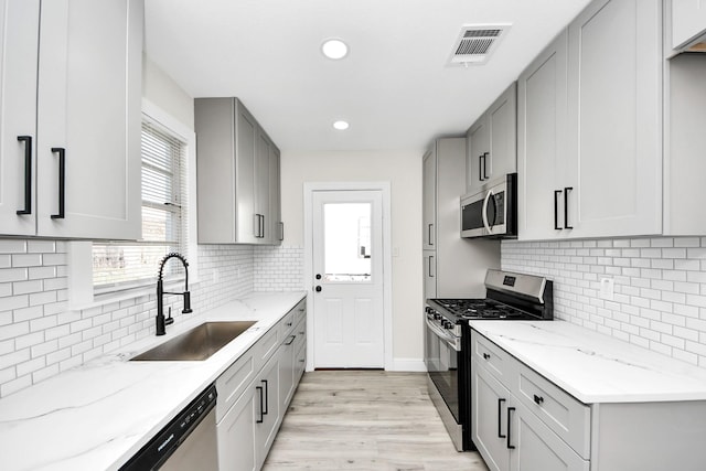 kitchen featuring visible vents, light stone countertops, gray cabinets, stainless steel appliances, and a sink