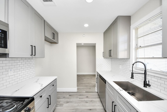 kitchen with light stone counters, gray cabinets, appliances with stainless steel finishes, a sink, and baseboards