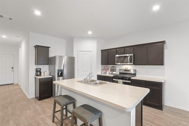 kitchen with appliances with stainless steel finishes, sink, dark brown cabinetry, light hardwood / wood-style floors, and a center island with sink