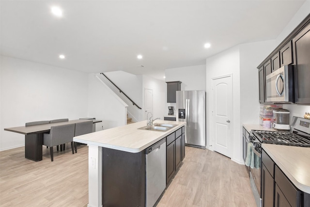 kitchen featuring sink, a kitchen island with sink, stainless steel appliances, dark brown cabinets, and light hardwood / wood-style flooring