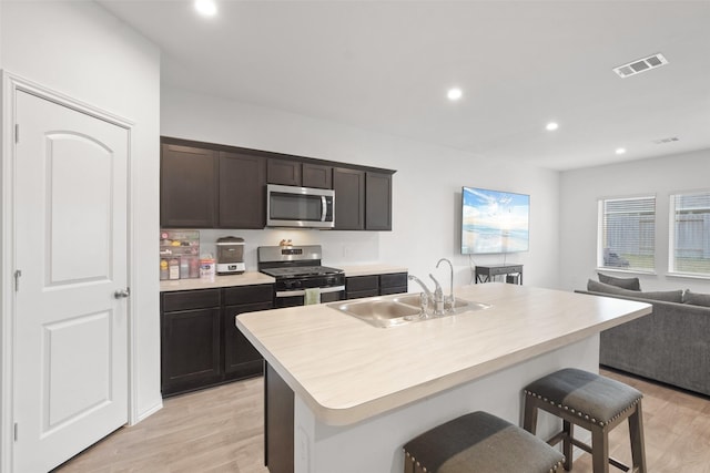 kitchen featuring sink, light hardwood / wood-style flooring, stainless steel appliances, a kitchen breakfast bar, and a center island with sink