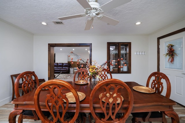 dining space with ceiling fan, ornamental molding, light hardwood / wood-style floors, and a textured ceiling