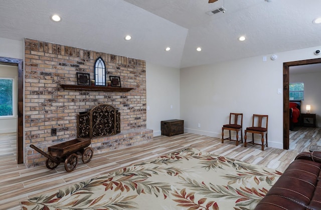 living room with a brick fireplace, vaulted ceiling, a textured ceiling, and light wood-type flooring