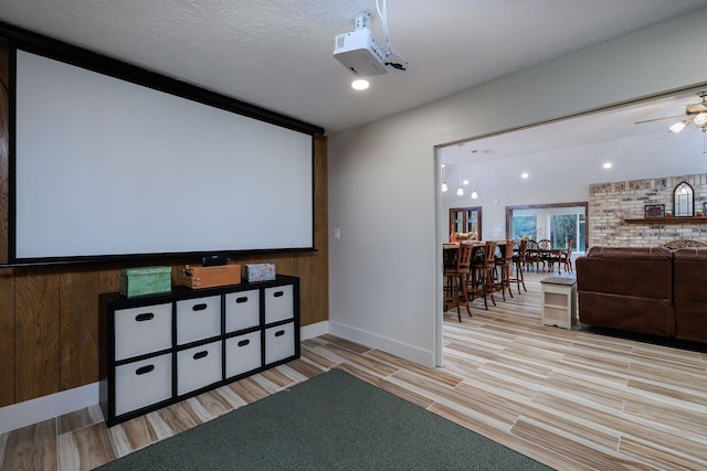 cinema room with ceiling fan, light hardwood / wood-style floors, and a textured ceiling