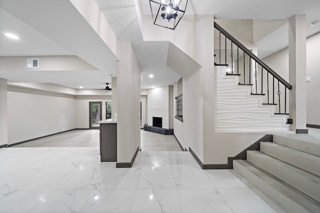 staircase with a large fireplace and ceiling fan